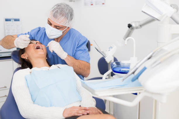 The dentist in face mask inspects female patient teeth with mirror and probe